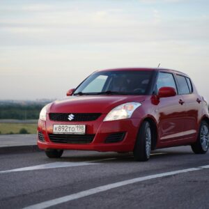 A red compact car on an asphalt road with a scenic backdrop near Saint Petersburg, Russia.